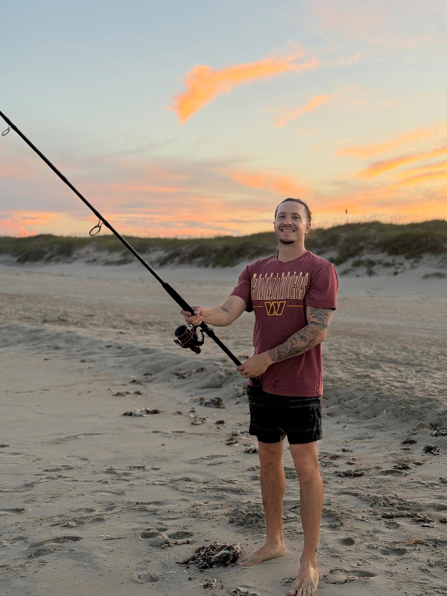 Shane smiling on the beach at sunset with a surf fishing rod